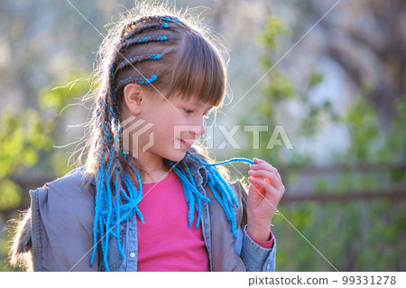Profile portrait of pretty smiling young teenager girl in casual clothes and blue ribbons plaited in long braids outdoors on summer or spring sunny day 99331278