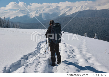 Man backpacker hiking snowy mountain hillside on cold winter day. Man backpacker hiking snowy mountain hillside on cold winter day. 99331697