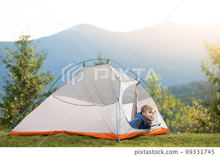 Hiker child boy resting sitting in a camping tent at mountains campsite enjoying view of summer nature. Hiker child boy resting sitting in a camping tent at mountains campsite enjoying view of summer nature. 99331745