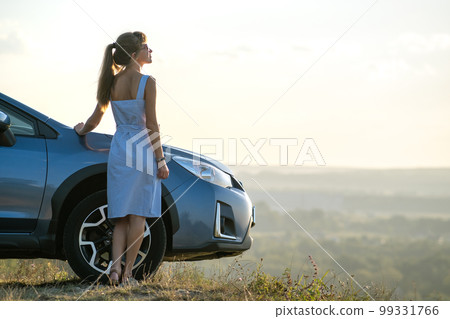 Happy young woman driver in blue dress leaning on her car enjoying warm summer day. Travelling and vacation concept. 99331766