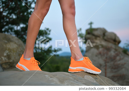 Closeup of young woman slim legs in bright orange sneaker shoes walking on mountain hiking trail in summer. Active way of life and exercise on fresh air concept. 99332084