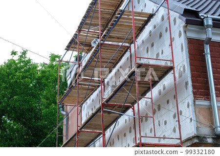 Building facade under renovation works with construction scaffolding frame. Wall insulation with styrofoam sheets for energy efficient home Building facade under renovation works with construction scaffolding frame. Wall insulation with styrofoam sheets for energy efficient home 99332180