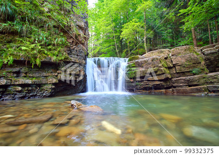 Amazing landscape of beautiful waterfall on mountain river with white foamy water falling down from rocky cliff in summer rainforest. 99332375