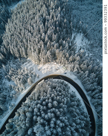 Aerial view of winter landscape with snow covered mountain hills and winding forest road in morning. 99332391