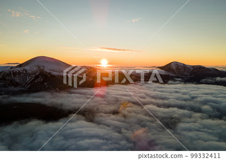 Aerial view of vibrant sunrise over white dense fog with distant dark Carpathian mountains on horizon. 99332411