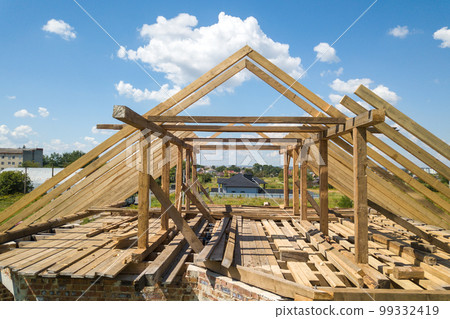 Aerial view of unfinished house with wooden roof frame structure under construction. 99332419