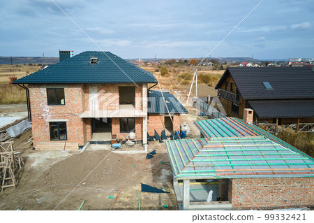 Aerial view of unfinished house with brick walls and wooden roof frame covered with metallic tiles under construction 99332421