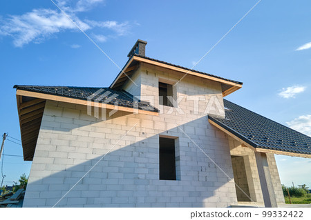 Aerial view of unfinished house with aerated lightweight concrete walls and wooden roof frame covered with metallic tiles under construction 99332422