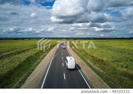 Aerial view of intercity road between green agricultural fields with fast driving cars. Top view from drone of highway traffic 99333132