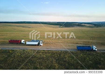Aerial view of cargo truck driving on dirt road between agricultural wheat fields making lot of dust. Transportation of grain after being harvested by combine harvester during harvesting season Aerial view of cargo truck driving on dirt road between agricultural wheat fields making lot of dust. Transportation of grain after being harvested by combine harvester during harvesting season 99333399
