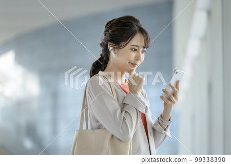 Business woman in her thirties wearing earphones looking at the screen of her smartphone 99338390