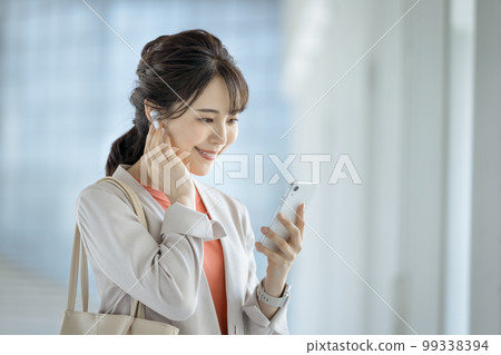 Business woman in her thirties wearing earphones looking at the screen of her smartphone 99338394