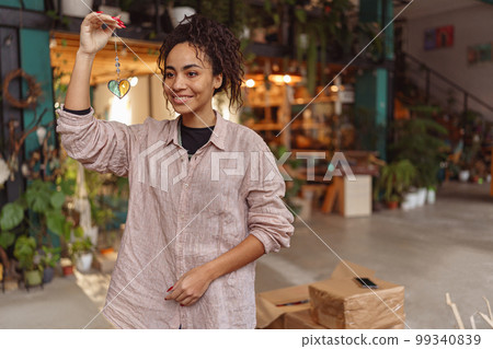 Smiling woman holding handmade glass decoration in the form of heart standing in home decor studio Smiling woman holding handmade glass decoration in the form of heart standing in home decor studio 99340839