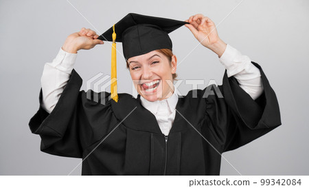 Smiling woman in graduation gown holding cap by tassel on white background.  99342084