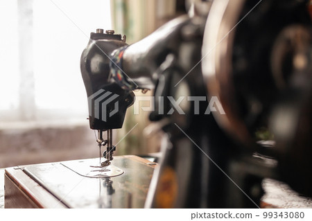 An old sewing machine stands on the table at home ready to work and sew. Classic retro style manual sewing machine ready for sewing work. The machine is old style made of metal with floral patterns An old sewing machine stands on the table at home ready to work and sew. Classic retro style manual sewing machine ready for sewing work. The machine is old style made of metal with floral patterns 99343080