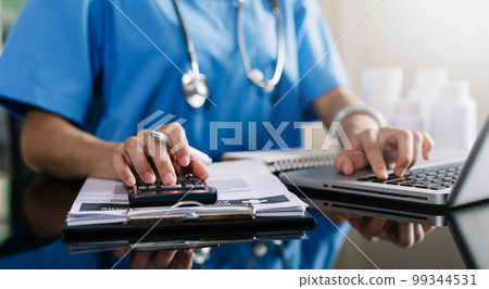 Healthcare costs and fees concept.Hand of smart doctor used a calculator and smartphone, tablet for medical costs at hospital in morning light 99344531