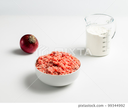 Plate with fresh ground beef and fork, red onion, measuring cup with flour on a white background, space for text, stock photo Plate with fresh ground beef and fork, red onion, measuring cup with flour on a white background, space for text, stock photo 99344992