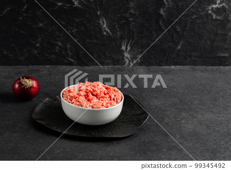 Plate with fresh ground beef, red onion on a gray black background, space for text, stock photo	 99345492