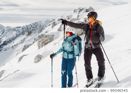 Couple of ski tourers looking at the views of the snowy Alps from high up Couple of ski tourers looking at the views of the snowy Alps from high up 99346545