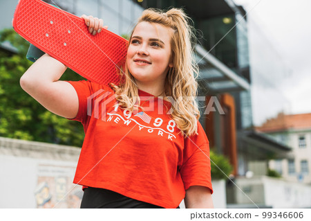 Waist up happy young girl with a red skate board on her shoulders Waist up happy young girl with a red skate board on her shoulders 99346606