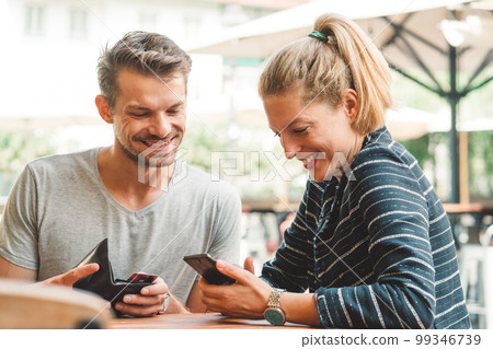 Young couple smiling while looking at their phone, sitting at a bar waiting for their drinks Young couple smiling while looking at their phone, sitting at a bar waiting for their drinks 99346739