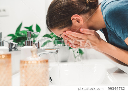 Close up side view woman leaning down in the sink washing her face with water  99346782
