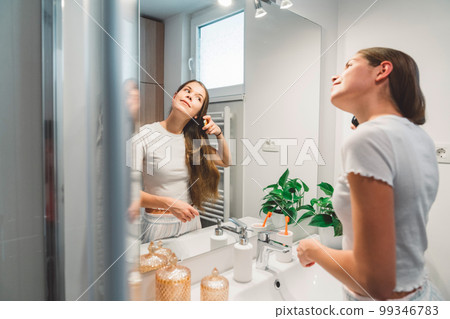 Side view of a woman brushing her long brown hair while looking at herself in the mirror Side view of a woman brushing her long brown hair while looking at herself in the mirror 99346783