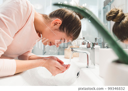 Woman closes her eyes while she washes her face with cold water in the morning Woman closes her eyes while she washes her face with cold water in the morning 99346832
