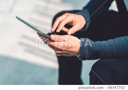 Man hands typing on digital tablet while sitting outside on a sunny day Man hands typing on digital tablet while sitting outside on a sunny day 99347783