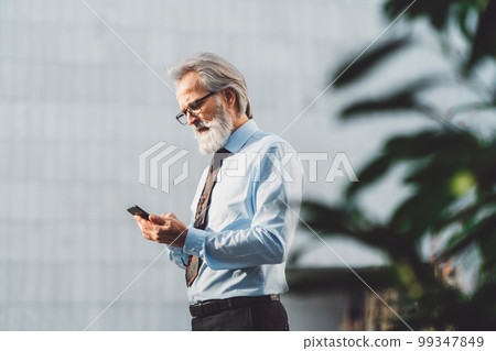 Waist up CEO, senior businessman standing outside the office building, making a phone call Waist up CEO, senior businessman standing outside the office building, making a phone call 99347849