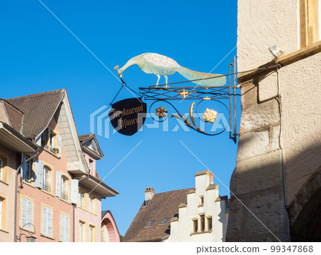 Biel, Switzerland - April 16th 2023: Restaurant signpost with a peafowl in front of historic buildings 99347868