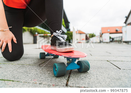 Close up unrecognizable young girl standing on her skateboard with one leg while kneeling down with the other Close up unrecognizable young girl standing on her skateboard with one leg while kneeling down with the other 99347875