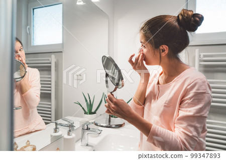 Side view of young woman cleaning her makeup in the bathcroom Side view of young woman cleaning her makeup in the bathcroom 99347893