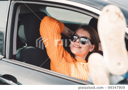 Young smiling woman enjoying life laying in her car while parked with her legs out of the window 99347909