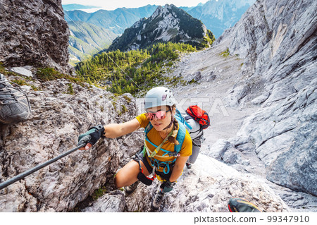 Smiling caucasian woman mountaineer with sunglasses on via ferrata trail in the Alps on a sunny summer day 99347910
