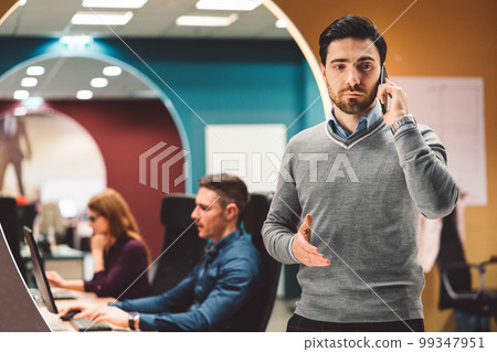 Young businessman having a business call, taking on the phone with a serious face expression Young businessman having a business call, taking on the phone with a serious face expression 99347951