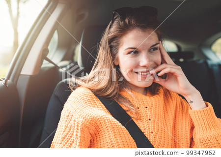 Young smiling woman leaning the head on her hand while driving in her car on the passenger seat 99347962