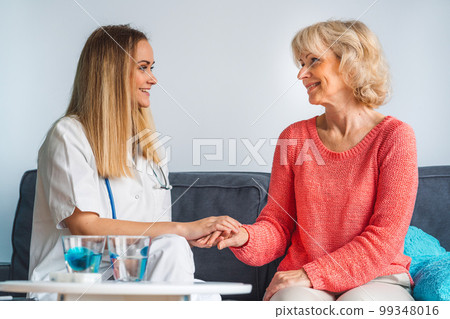 Nurse holding hands with senior lady while sitting on the couch, young caregiver loves helping people in need 99348016