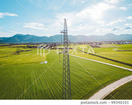 Sun is shining trough the clouds over the electrical tower in the middle of agricultural fields in the country side  99348101