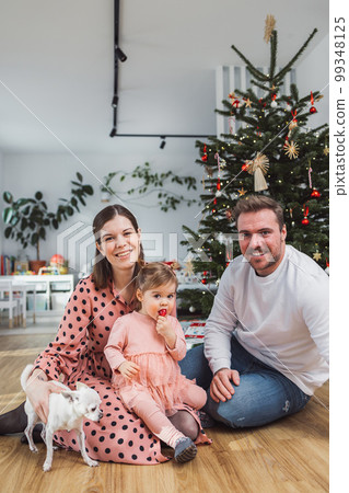 Vertical portrait of young caucasian family with baby girl and a chihuahua in front of the Christmas tree Vertical portrait of young caucasian family with baby girl and a chihuahua in front of the Christmas tree 99348125