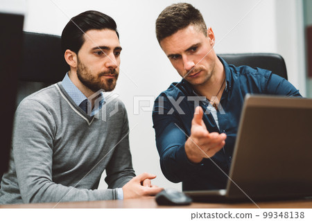 Couple of colleagues at a start up company working on laptop discussing an issue that needs to be solved  99348138