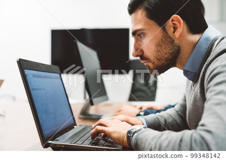 Side view of a focused business man leaning in closer to the laptop screen, coding  99348142