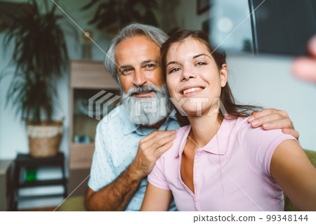 Smiling young woman and senior man her grandfather taking a selfie together Smiling young woman and senior man her grandfather taking a selfie together 99348144