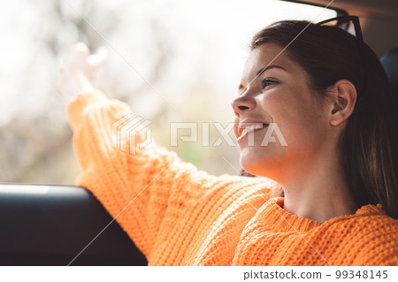 Side portrait waist up young woman sitting in her car looking out the window with a smile on her face Side portrait waist up young woman sitting in her car looking out the window with a smile on her face 99348145