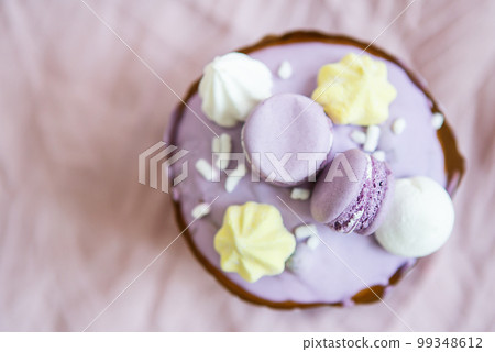 A traditional paska decorated with white Swiss chocolate and meringue stands on a lavender tablecloth. Easter holiday, top view. Place for inscription. 99348612