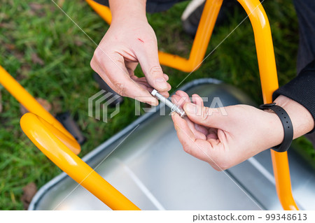 A metal wheelbarrow stands on the street, a man twists a new wheelbarrow for work, twists bolts and nuts. 99348613