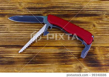 Red all purpose pocket knife on a rustic wooden background. Top view 99348886