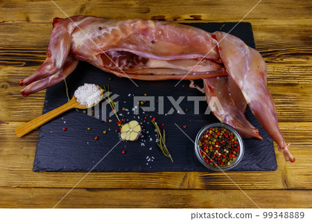 Whole raw rabbit meat with spices on a black slate cutting board on wooden table Whole raw rabbit meat with spices on a black slate cutting board on wooden table 99348889