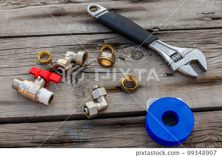Various plumbing spare parts, sealing tape and adjustable wrench on rustic wooden background. Top view Various plumbing spare parts, sealing tape and adjustable wrench on rustic wooden background. Top view 99348907