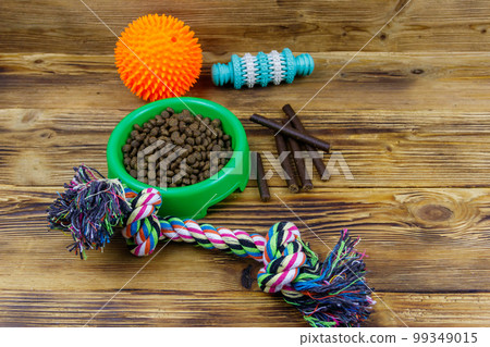 Dog toys and feed for dogs in green plastic bowl on wooden background. Dog care concept Dog toys and feed for dogs in green plastic bowl on wooden background. Dog care concept 99349015